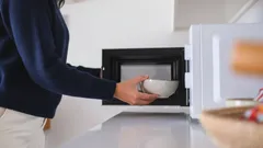 Person värmer mat i mikrovågsugn på modernt kök. Vit skål och öppen mikrougn.
